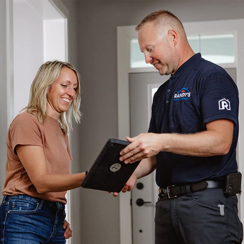 A Randy's Electric employee showing a tablet to a smiling woman in a home setting.