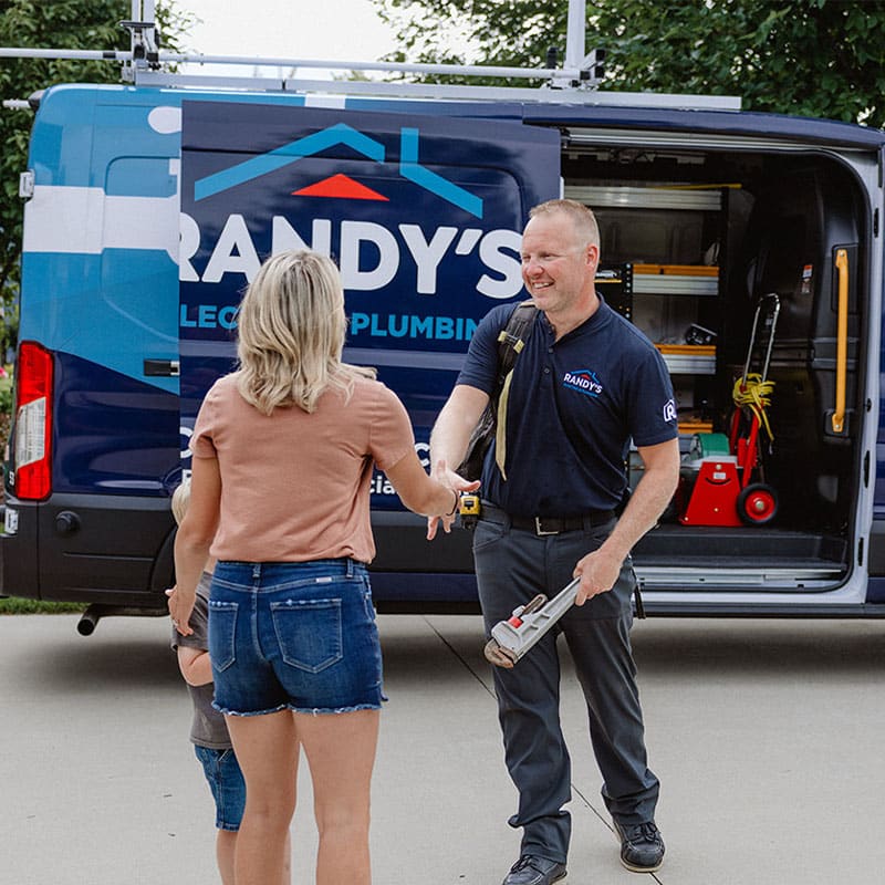 Plumber from Randy's Plumbing shakes hands with a woman in front of a service van.