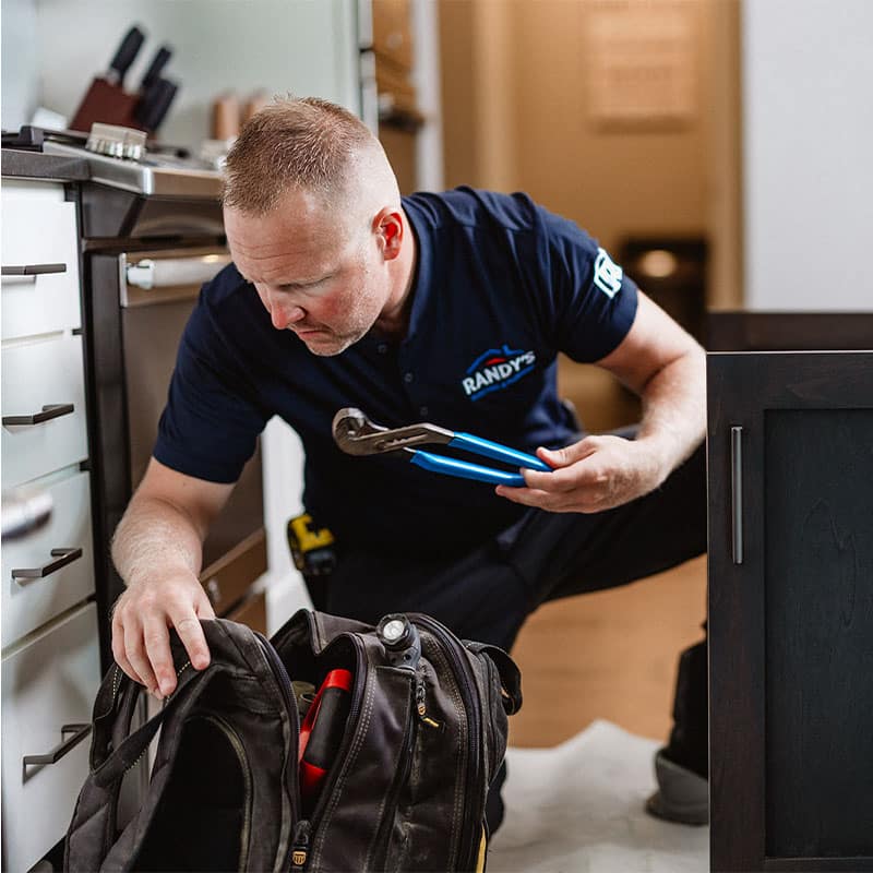 A plumber checking tools in a kitchen, wearing a Randy's uniform and holding a wrench.